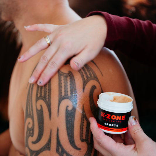 Person applying a tub of X-Zone Sports cream to a tattooed arm.