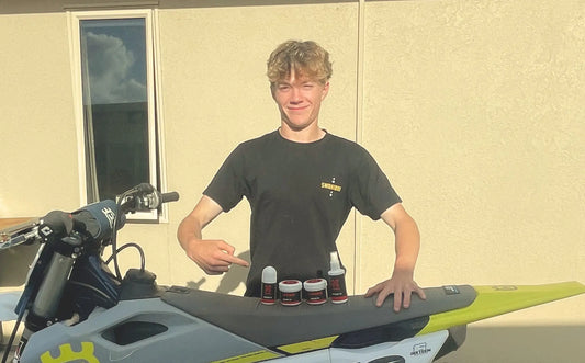 Ash McCormick standing behind Motorcross bike with X-ZONE Sports products on the seat