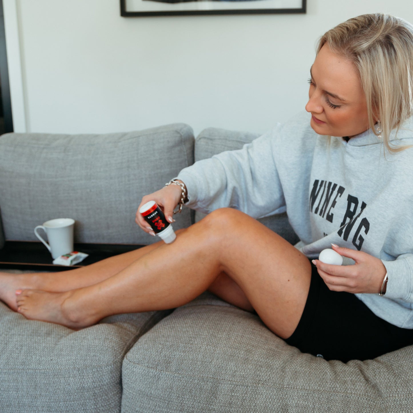 Woman sitting on a couch applying X-Zone Sports Roll on to her leg in a living room.