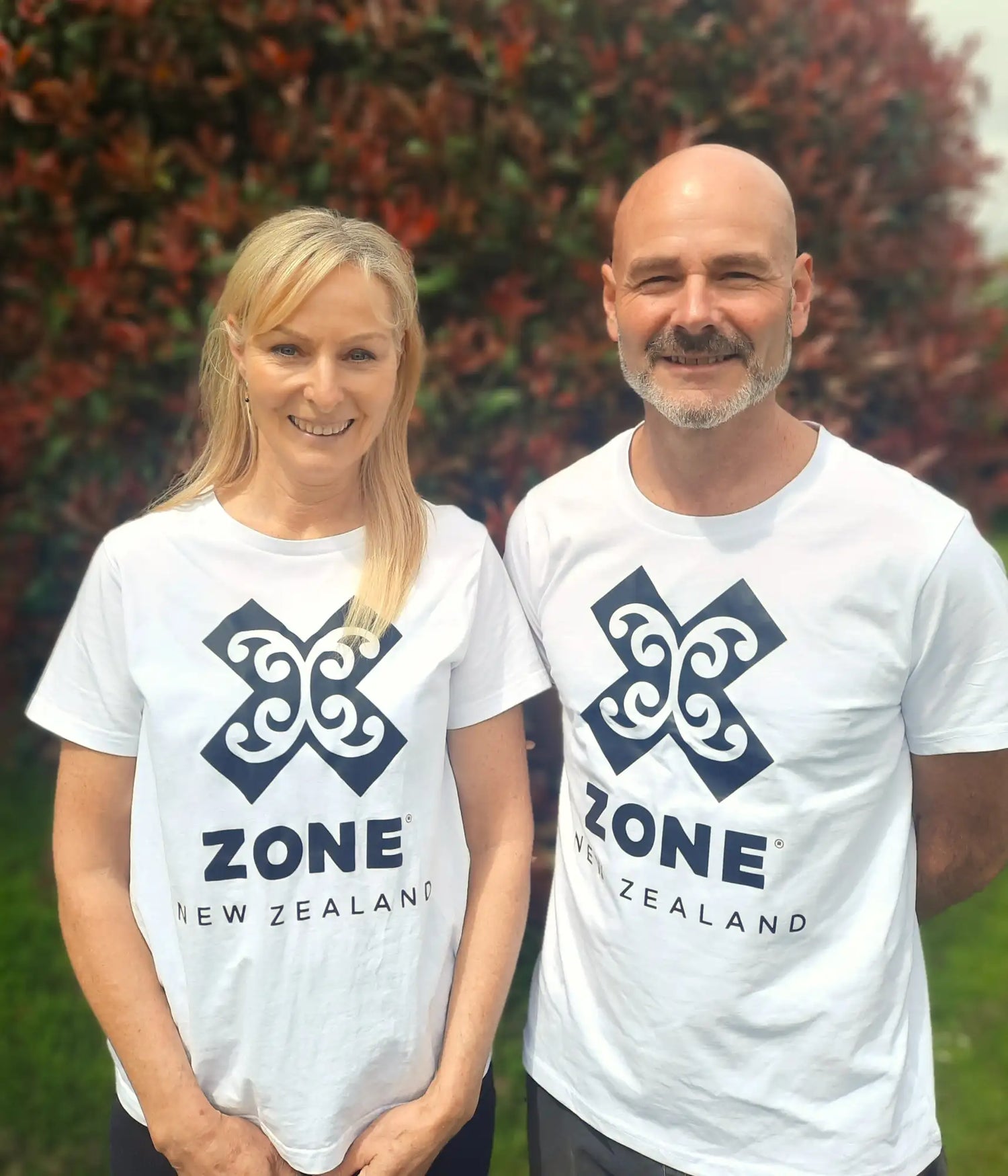 White cotton t-shirt featuring a navy blue maori-style design with ’zone new zealand’ printed below