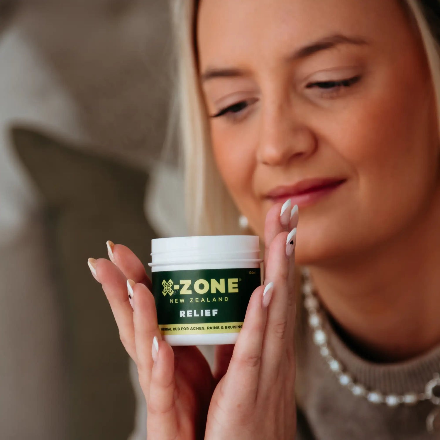 A white cylindrical jar with a green label featuring the ’z-one new zealand relief’ branding, containing an herbal rub for achilles pains and bruising.